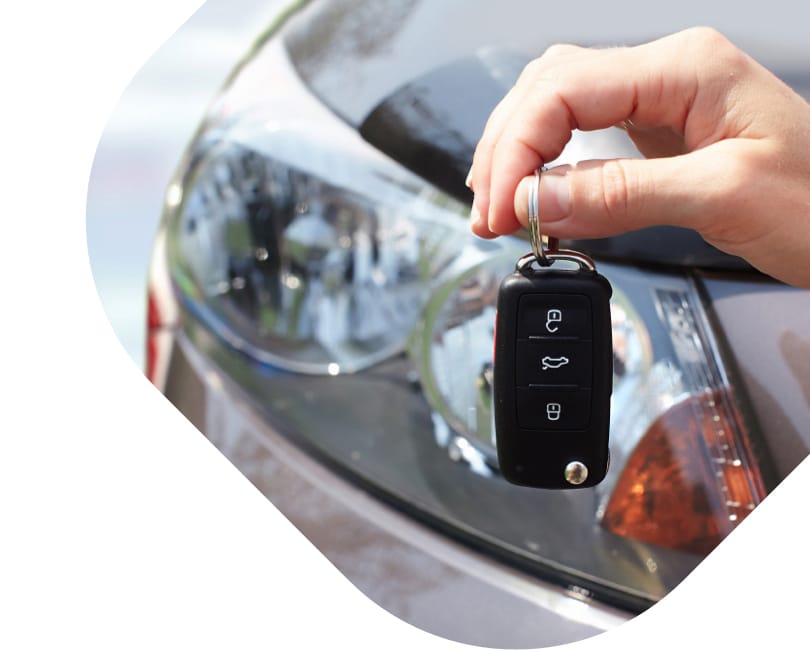 A set of car keys being held in front of a used vehicle.